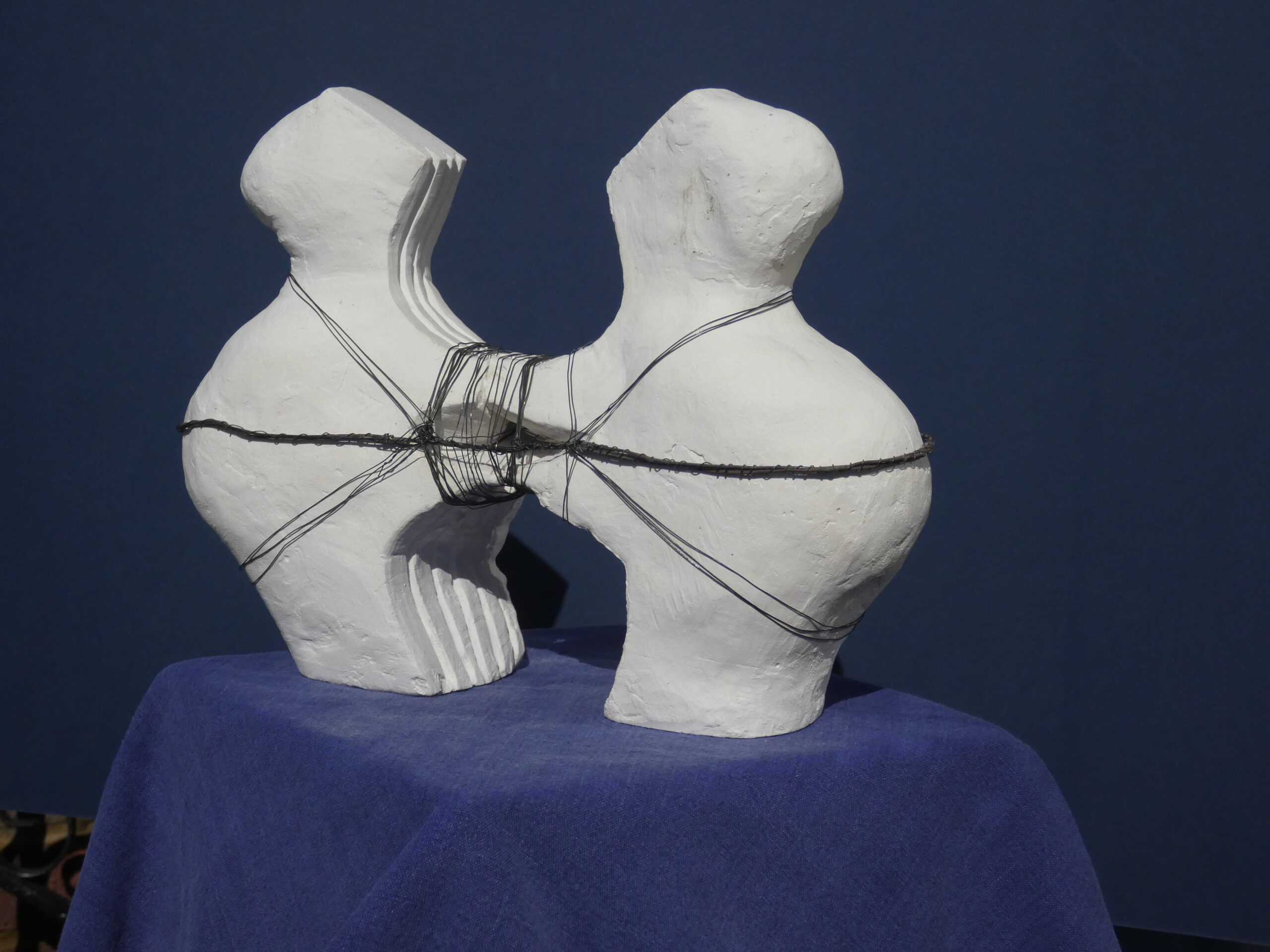 Plaster sculpture of two stylised people pulling away from each other bound together with wire